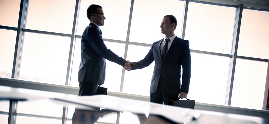 Silhouettes of two businessmen standing by the window and handshaking